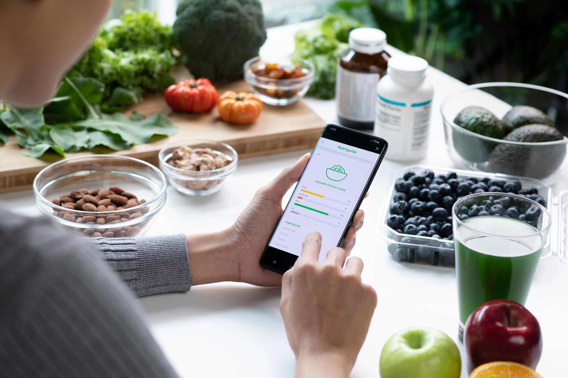 Woman Asian Professional Nutritionist busy working and checking data from a phone with a variety of fruits, nuts, vegetables, and dietary supplements on the table